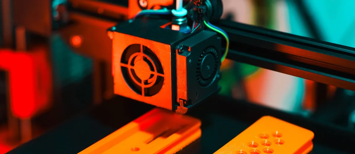 Impressora 3D produzindo um keyguard verde na oficina maker, com carretel de filamento e peças prontas na bancada